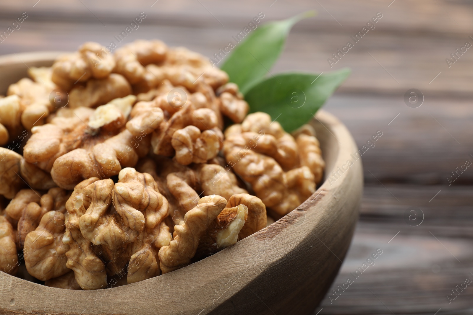 Photo of Peeled walnuts in bowl on wooden table, closeup