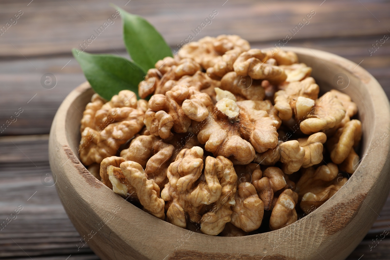 Photo of Peeled walnuts and green leaves in bowl on table, closeup