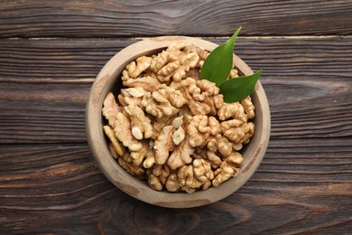 Photo of Peeled walnuts and green leaves in bowl on wooden table, top view