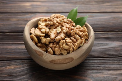 Photo of Peeled walnuts and green leaves in bowl on wooden table, closeup