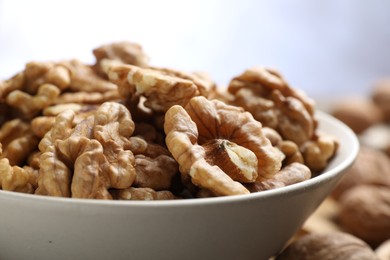 Photo of Peeled walnuts in bowl on table against light background, closeup