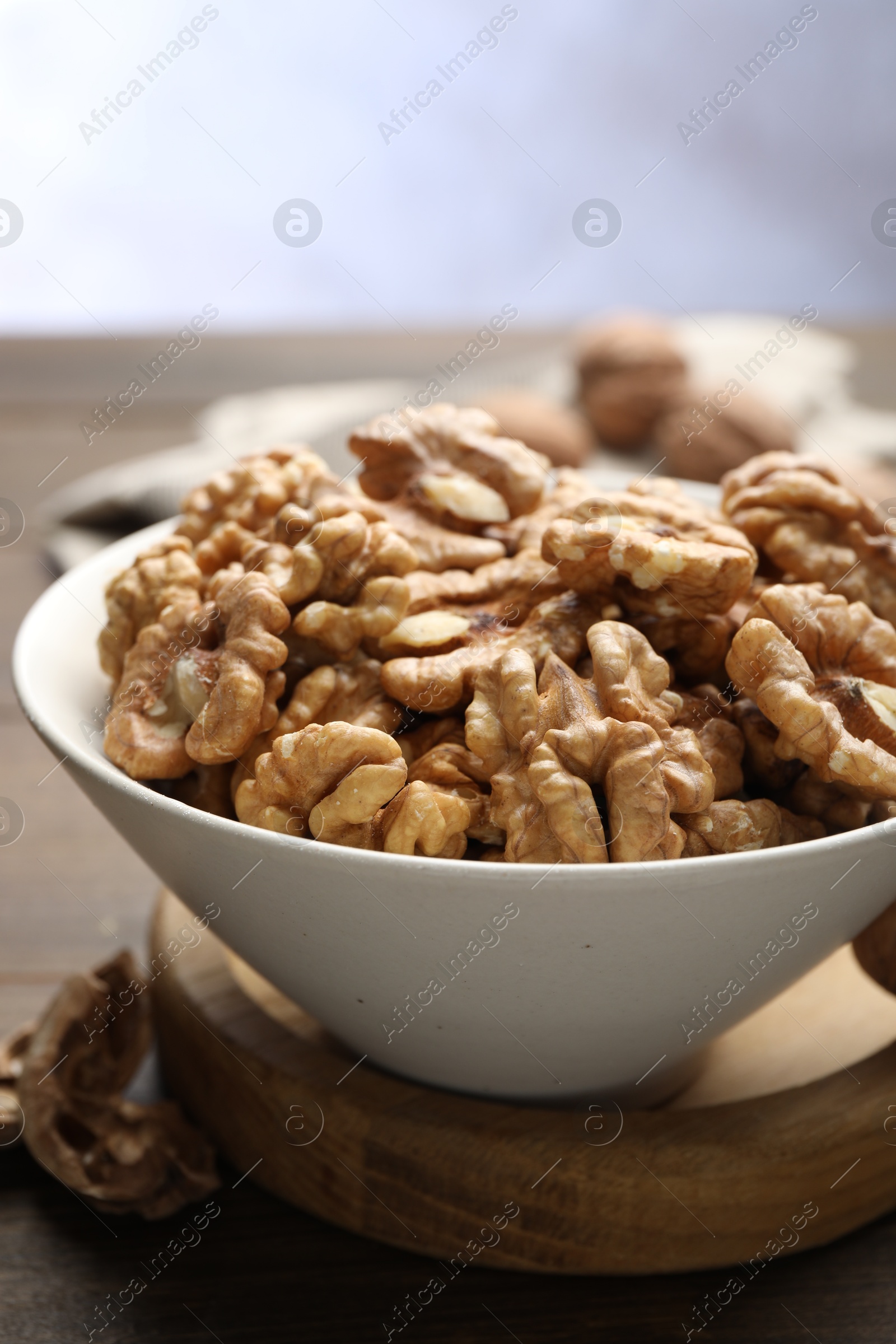 Photo of Peeled walnuts in bowl on table against light background, closeup