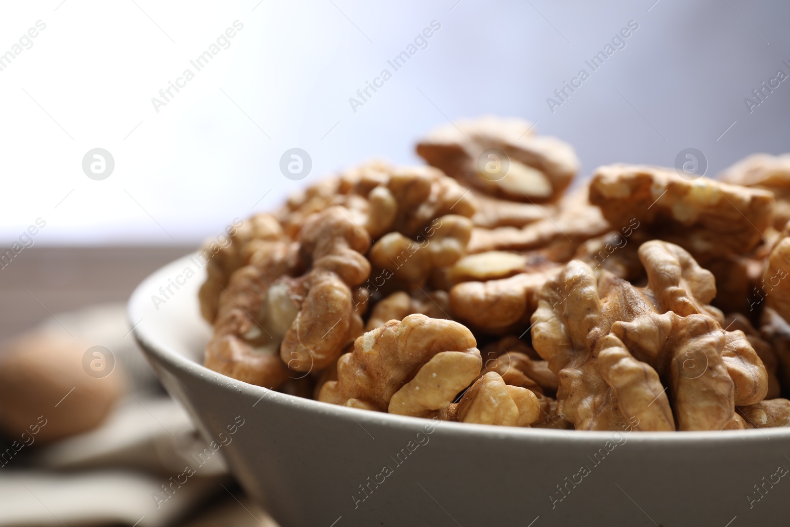 Photo of Peeled walnuts in bowl on table against light background, closeup