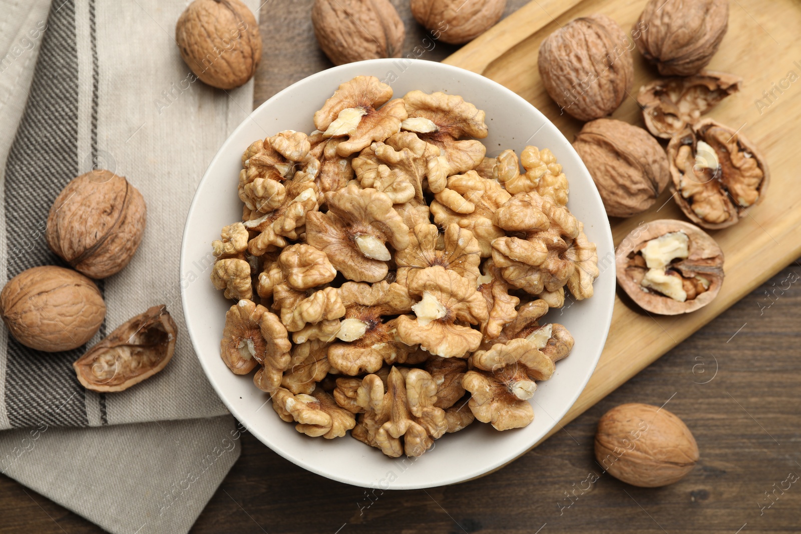 Photo of Peeled walnuts in bowl on wooden table, flat lay