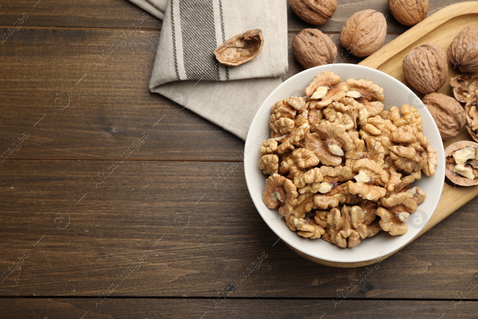 Photo of Peeled walnuts in bowl on wooden table, flat lay. Space for text