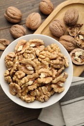 Photo of Peeled walnuts in bowl on wooden table, flat lay