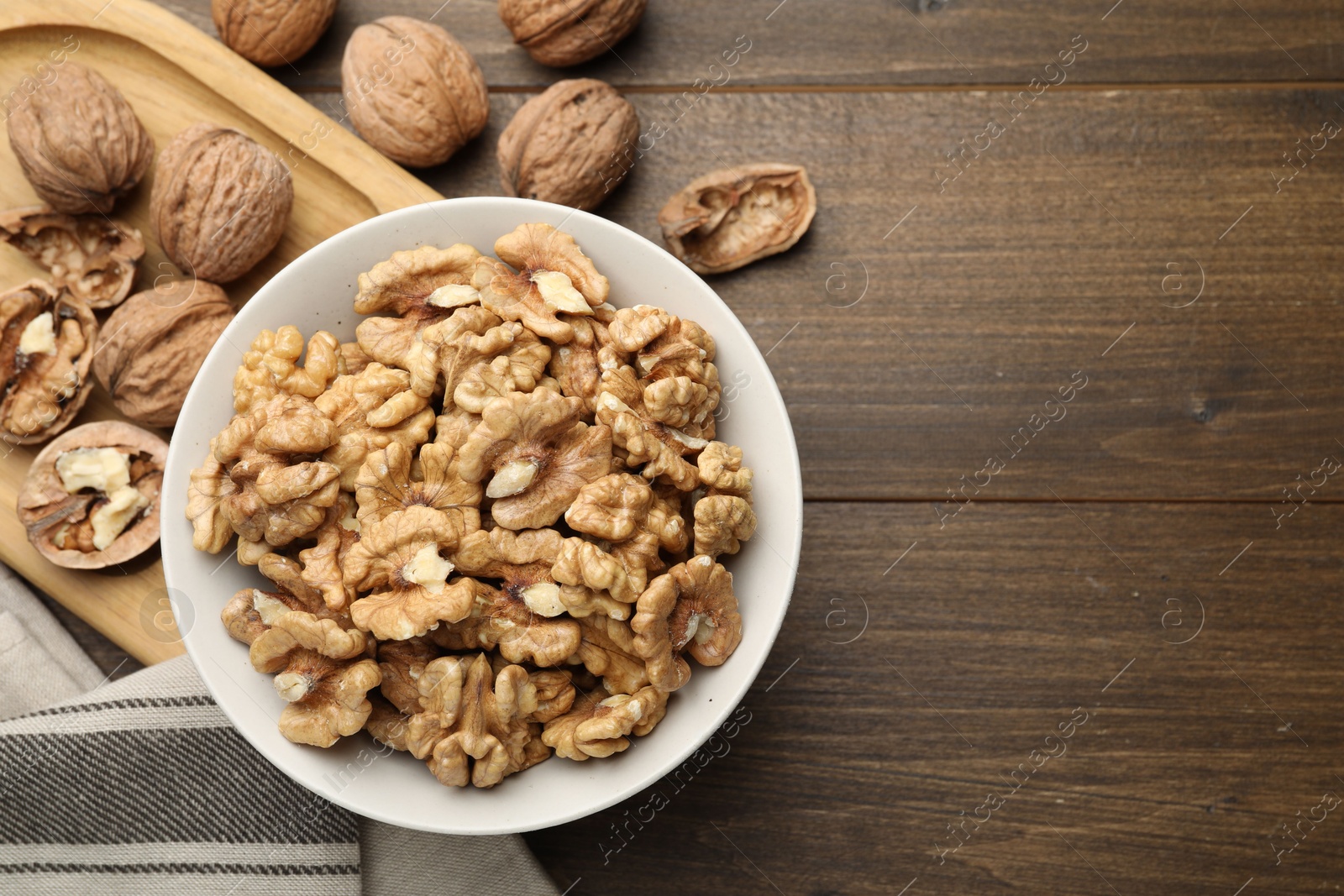 Photo of Peeled walnuts in bowl on wooden table, flat lay. Space for text