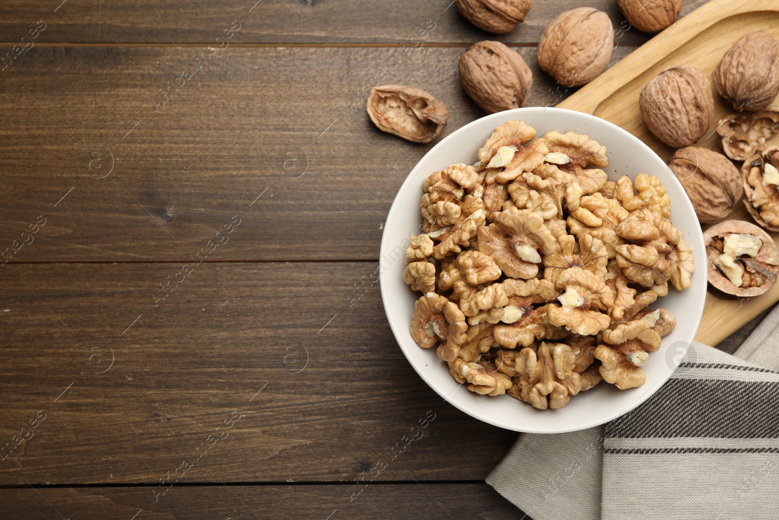 Photo of Peeled walnuts in bowl on wooden table, flat lay. Space for text