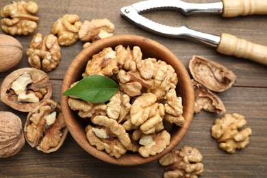 Photo of Peeled walnuts in bowl and nutcracker on wooden table, flat lay