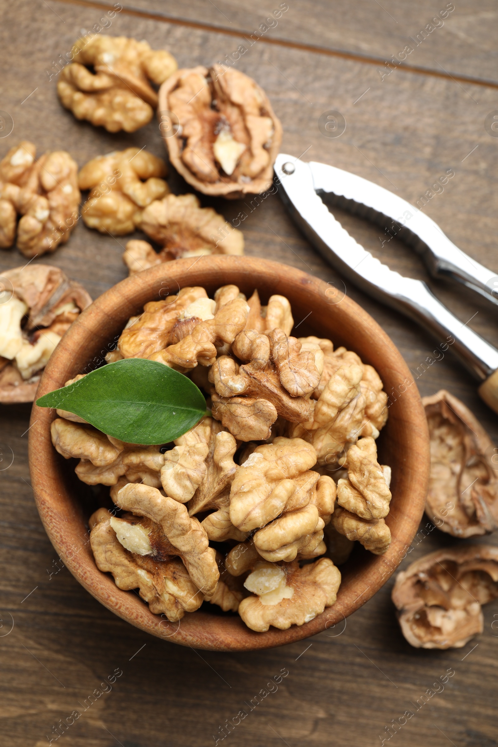 Photo of Peeled walnuts in bowl and nutcracker on wooden table, flat lay