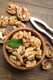 Photo of Peeled walnuts in bowl and nutcracker on wooden table, flat lay