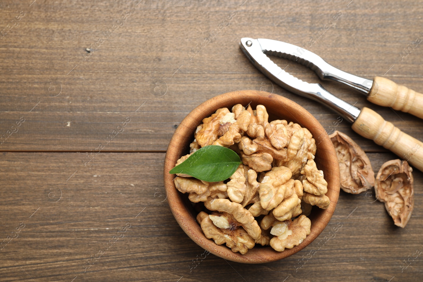 Photo of Peeled walnuts in bowl and nutcracker on wooden table, flat lay. Space for text