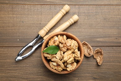 Photo of Peeled walnuts in bowl and nutcracker on wooden table, flat lay