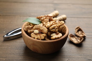 Photo of Peeled walnuts in bowl and nutcracker on wooden table, closeup