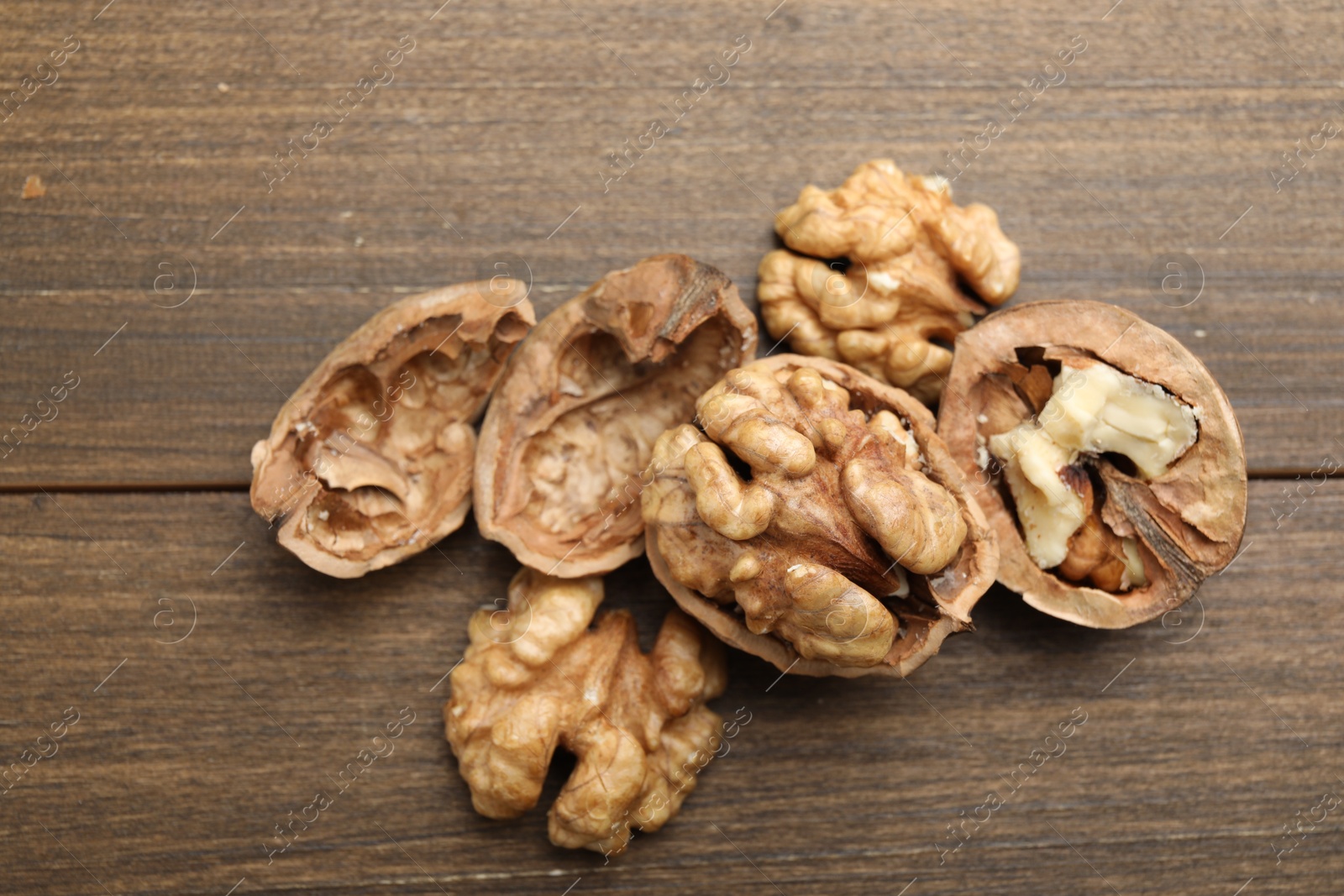 Photo of Fresh walnuts with shells on wooden table, flat lay