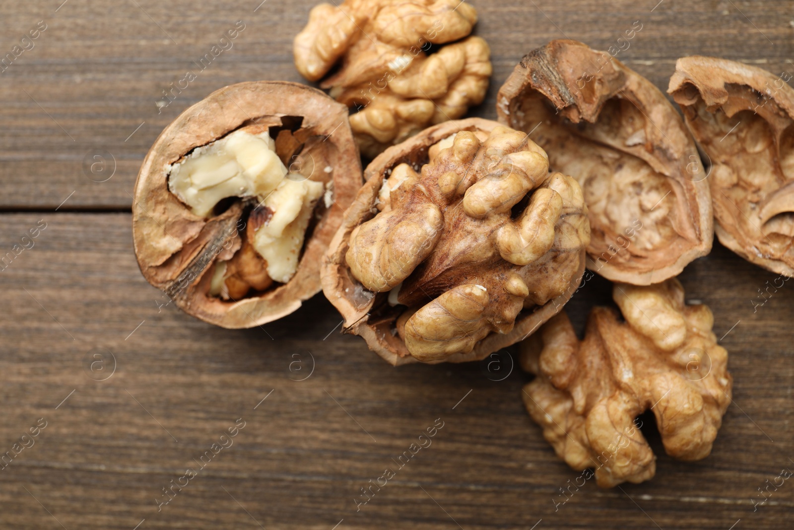 Photo of Fresh walnuts with shells on wooden table, flat lay