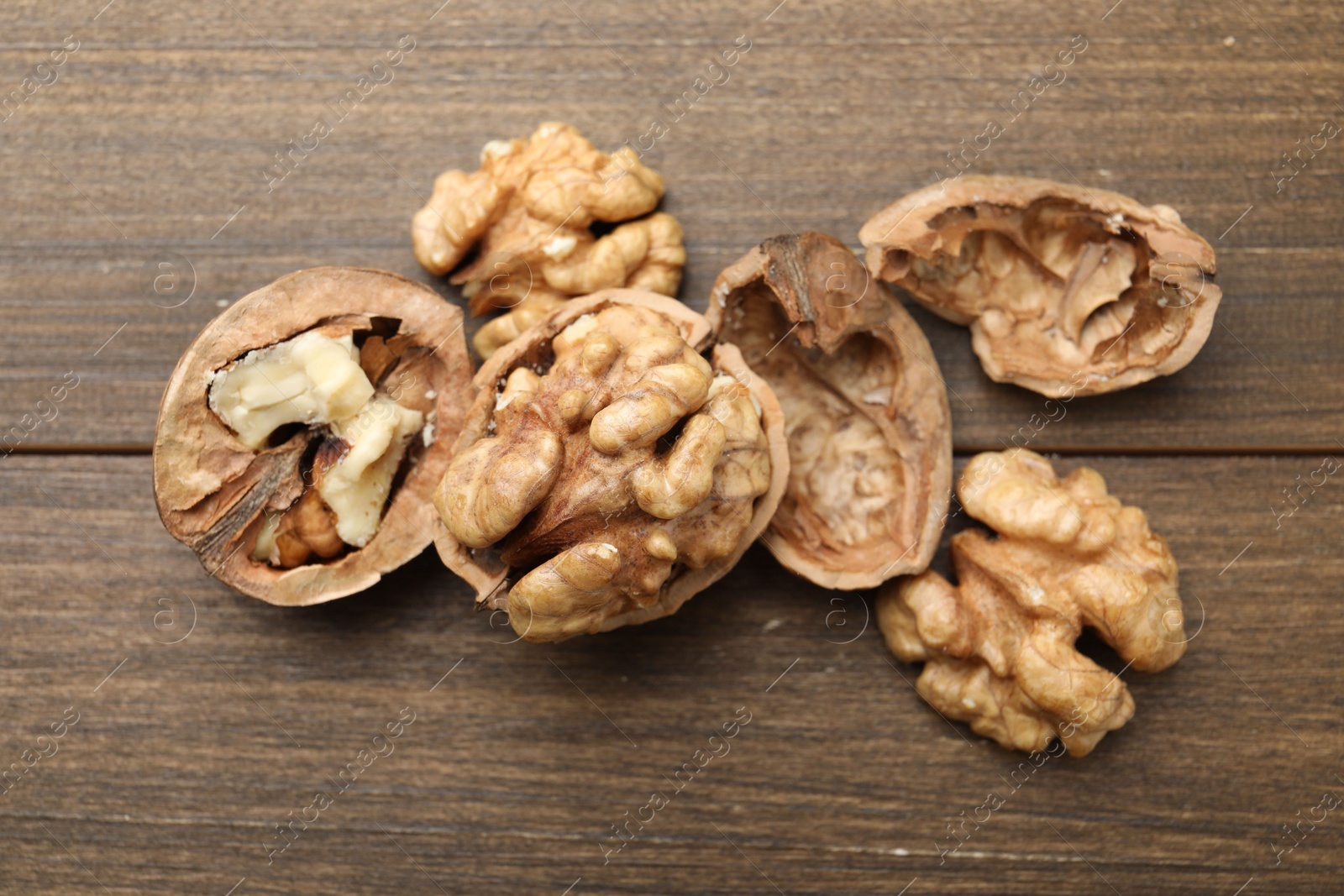 Photo of Fresh walnuts with shells on wooden table, flat lay