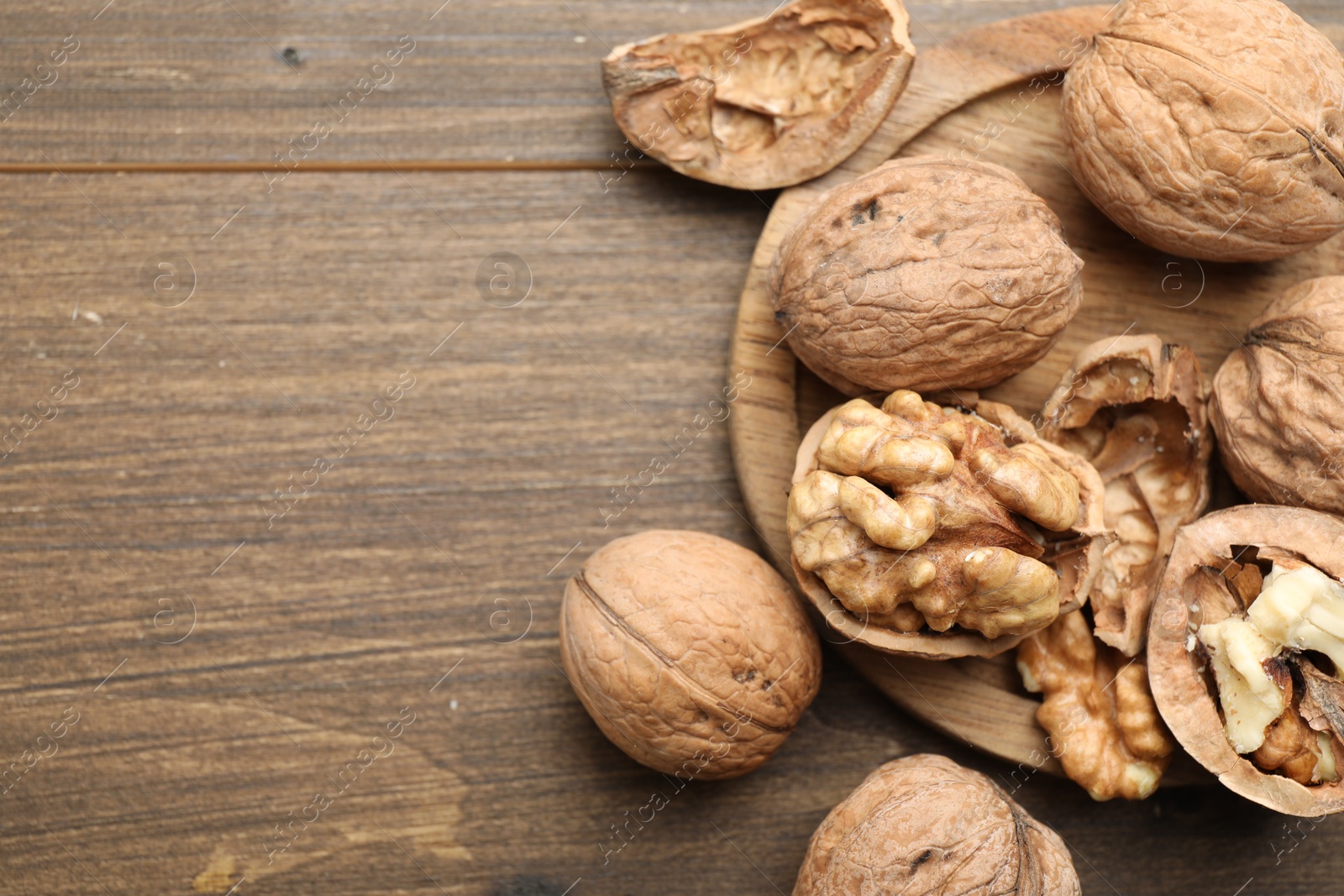 Photo of Fresh walnuts with shells on wooden table, flat lay. Space for text