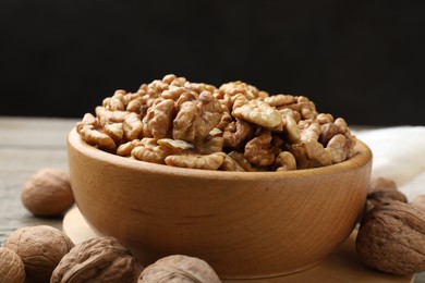 Photo of Peeled walnuts in bowl and whole ones on wooden table, closeup