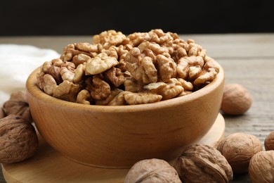 Photo of Peeled walnuts in bowl and whole ones on wooden table, closeup