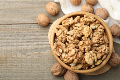 Photo of Peeled walnuts in bowl and whole ones on wooden table, flat lay. Space for text