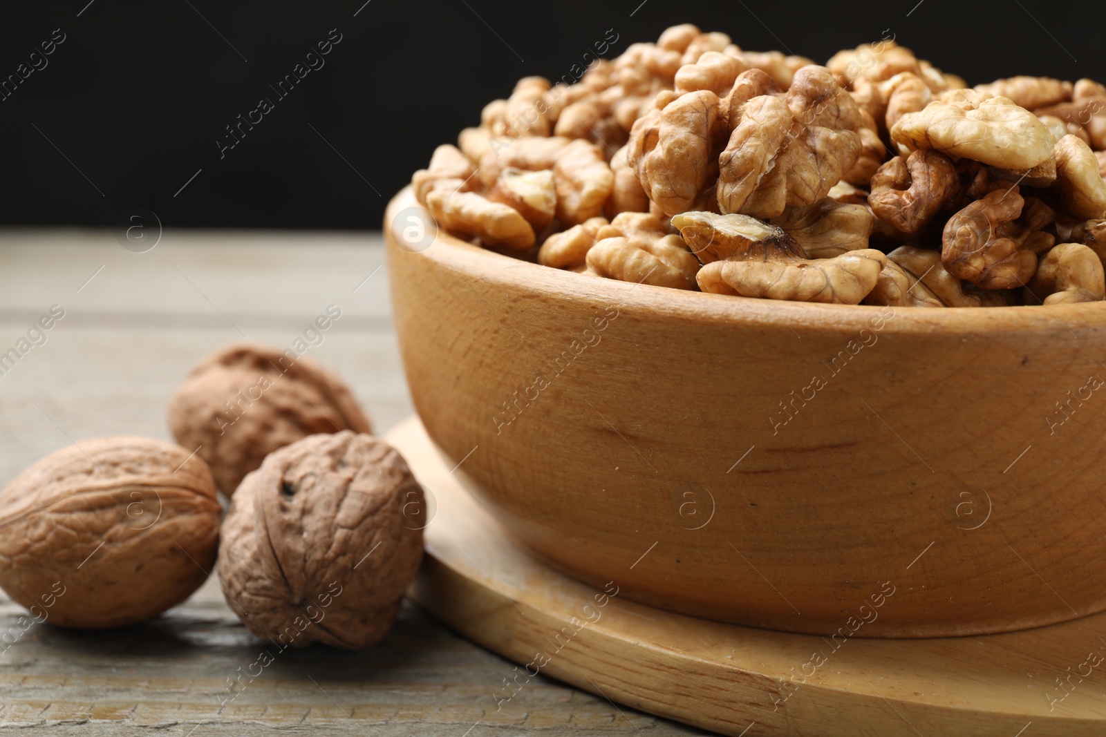 Photo of Peeled walnuts in bowl and whole ones on wooden table, closeup