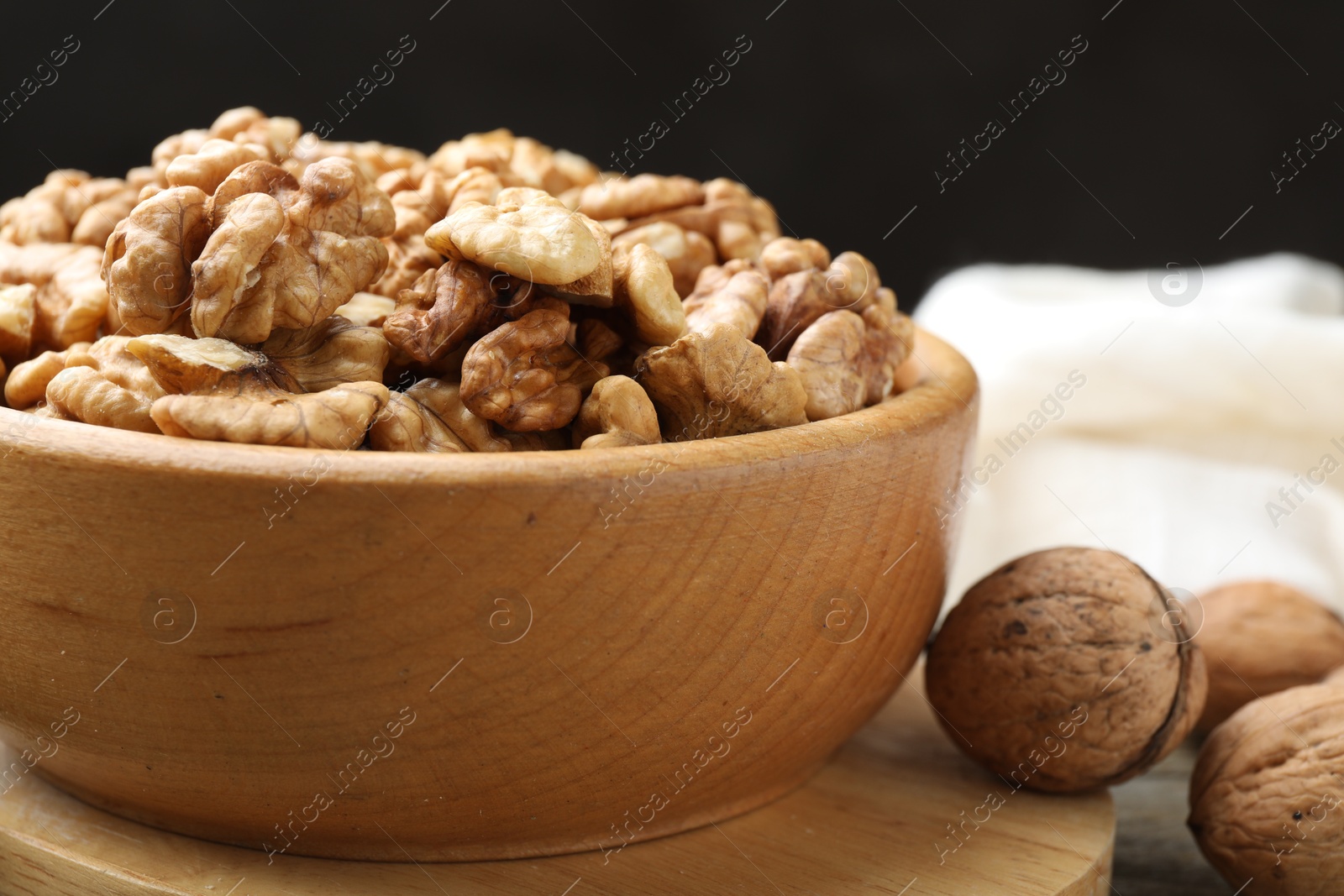 Photo of Peeled walnuts in bowl and whole ones on table, closeup