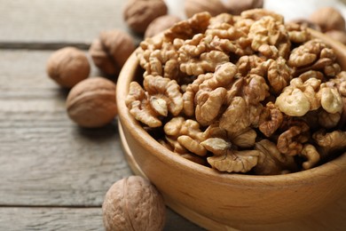 Photo of Peeled walnuts in bowl and whole ones on wooden table, closeup. Space for text