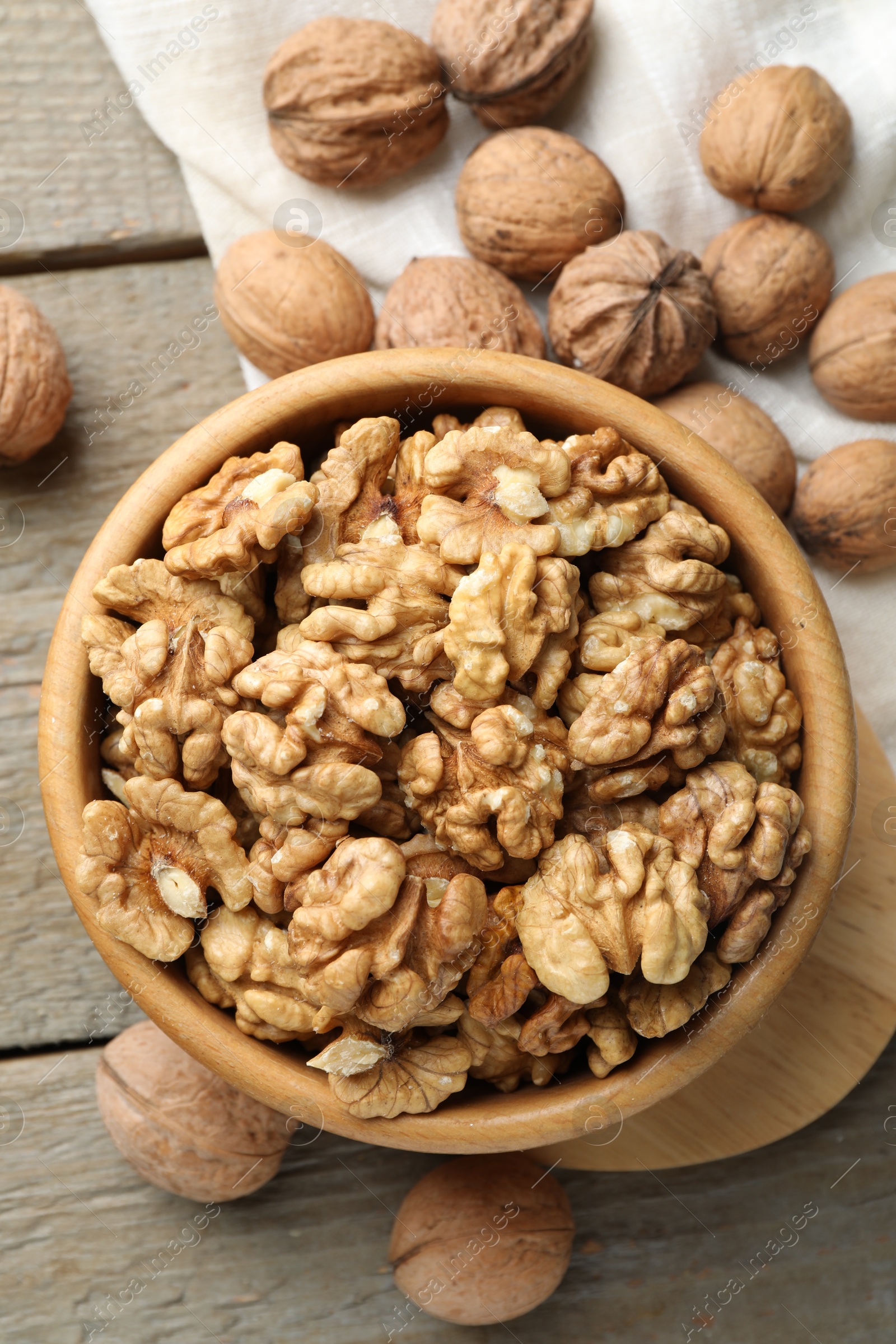 Photo of Peeled walnuts in bowl and whole ones on wooden table, flat lay