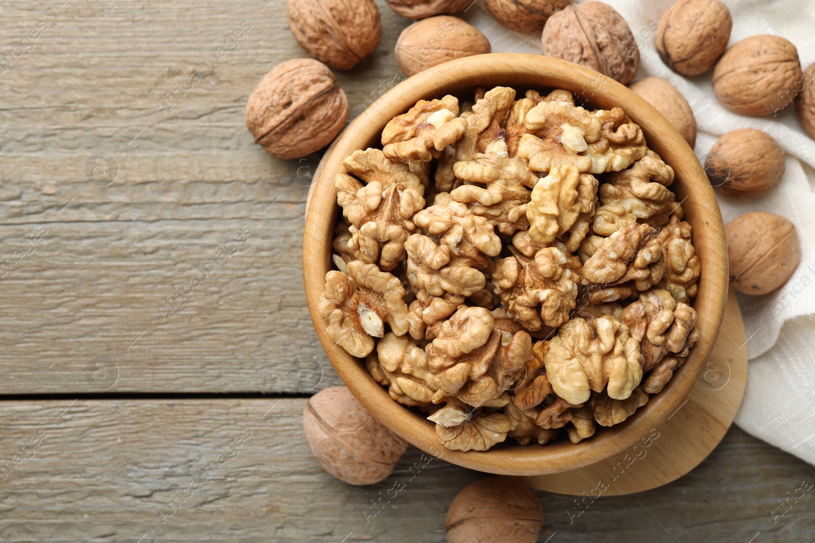 Photo of Peeled walnuts in bowl and whole ones on wooden table, flat lay. Space for text