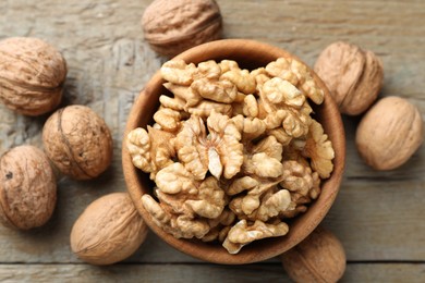 Photo of Peeled walnuts in bowl and whole ones on wooden table, flat lay