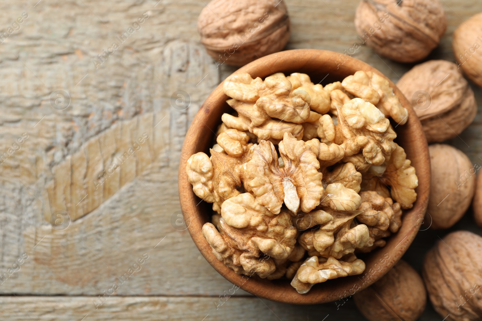 Photo of Peeled walnuts in bowl and whole ones on wooden table, flat lay. Space for text