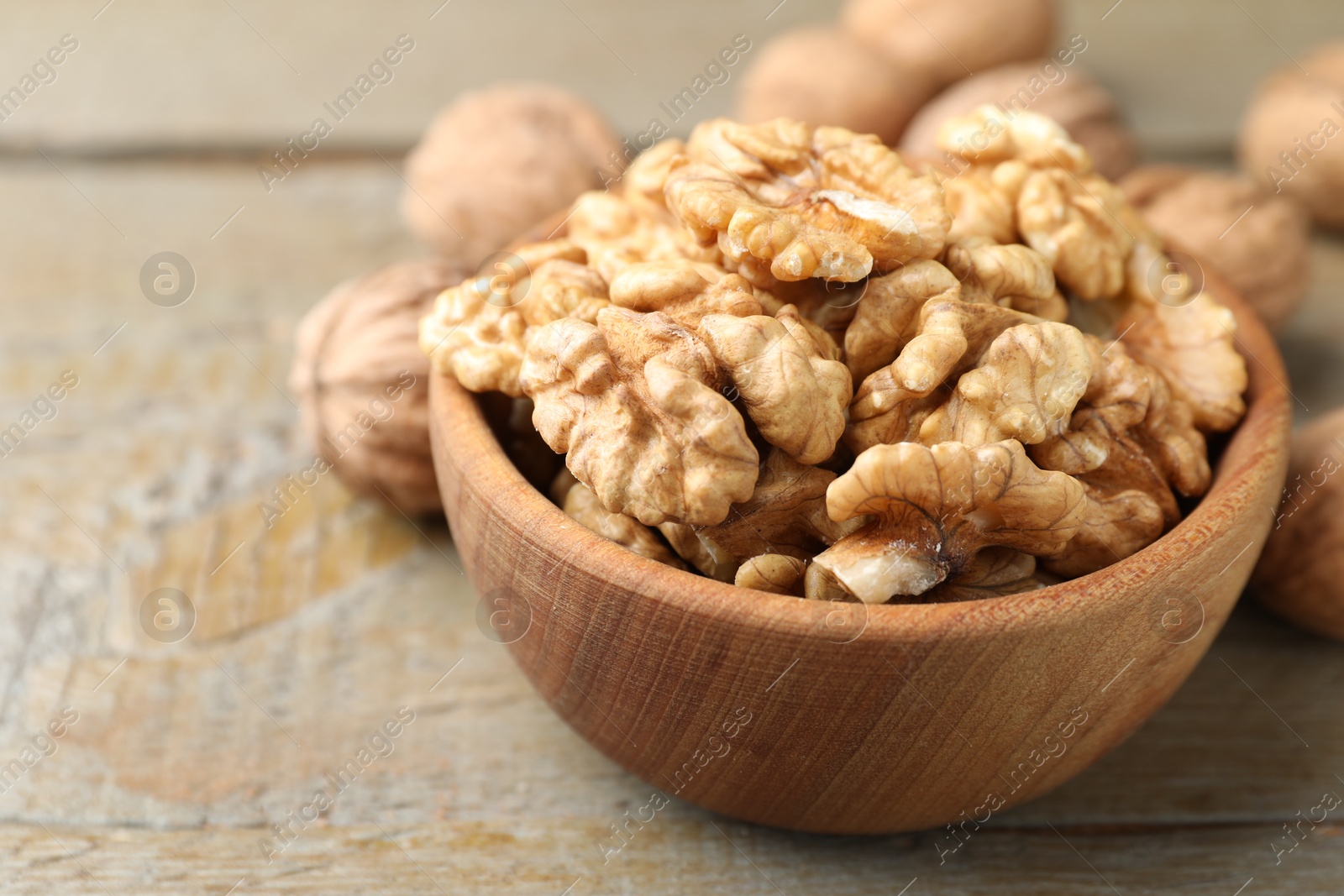 Photo of Peeled walnuts in bowl on wooden table, closeup. Space for text