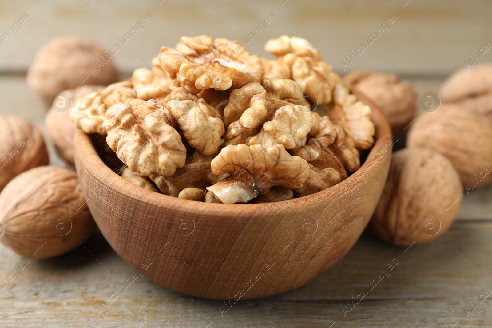 Photo of Peeled walnuts in bowl and whole ones on wooden table, closeup