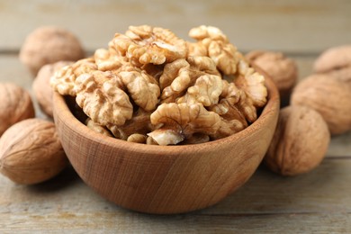 Photo of Peeled walnuts in bowl and whole ones on wooden table, closeup