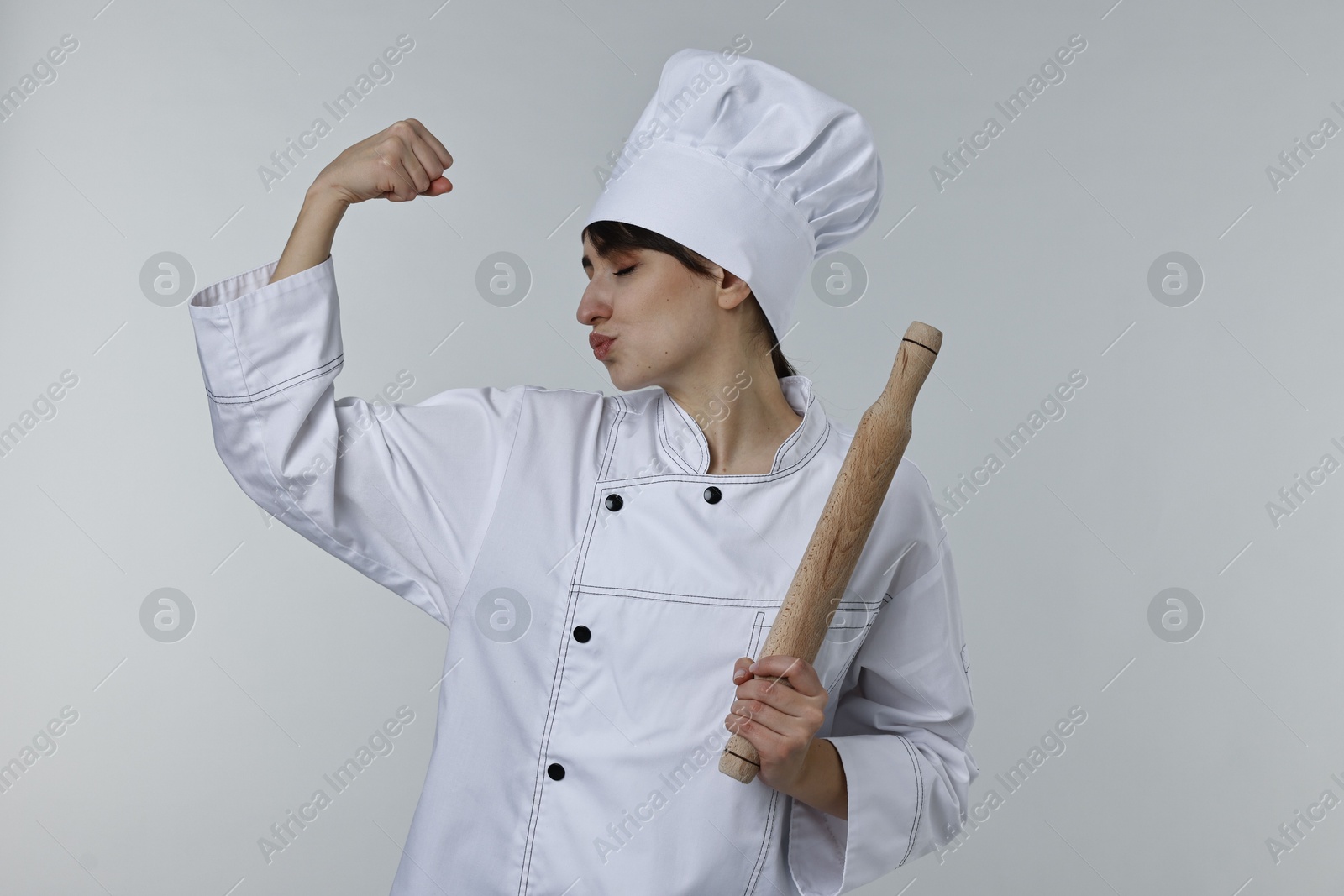 Photo of Professional chef with rolling pin kissing bicep on light grey background