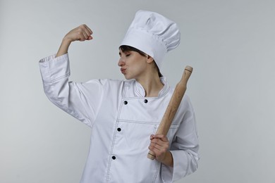 Photo of Professional chef with rolling pin kissing bicep on light grey background