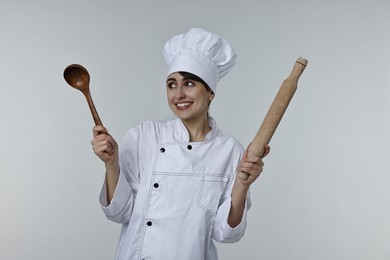 Photo of Professional chef with rolling pin and ladle on light grey background