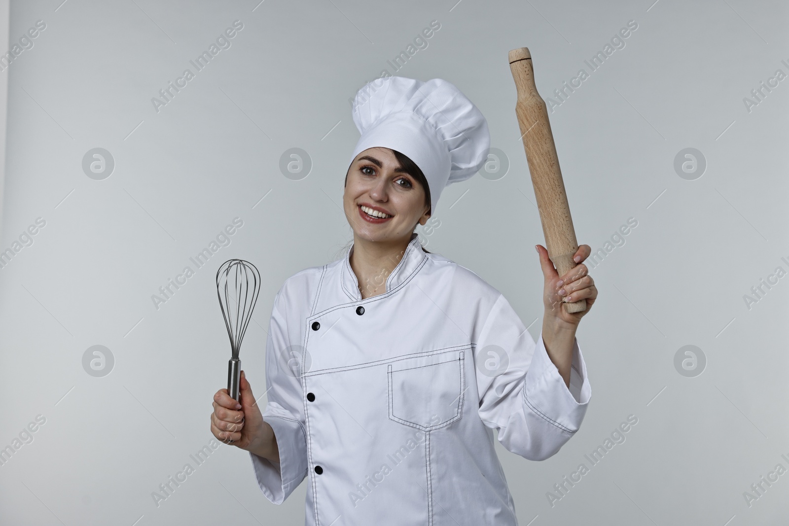 Photo of Professional chef with rolling pin and whisk on light grey background