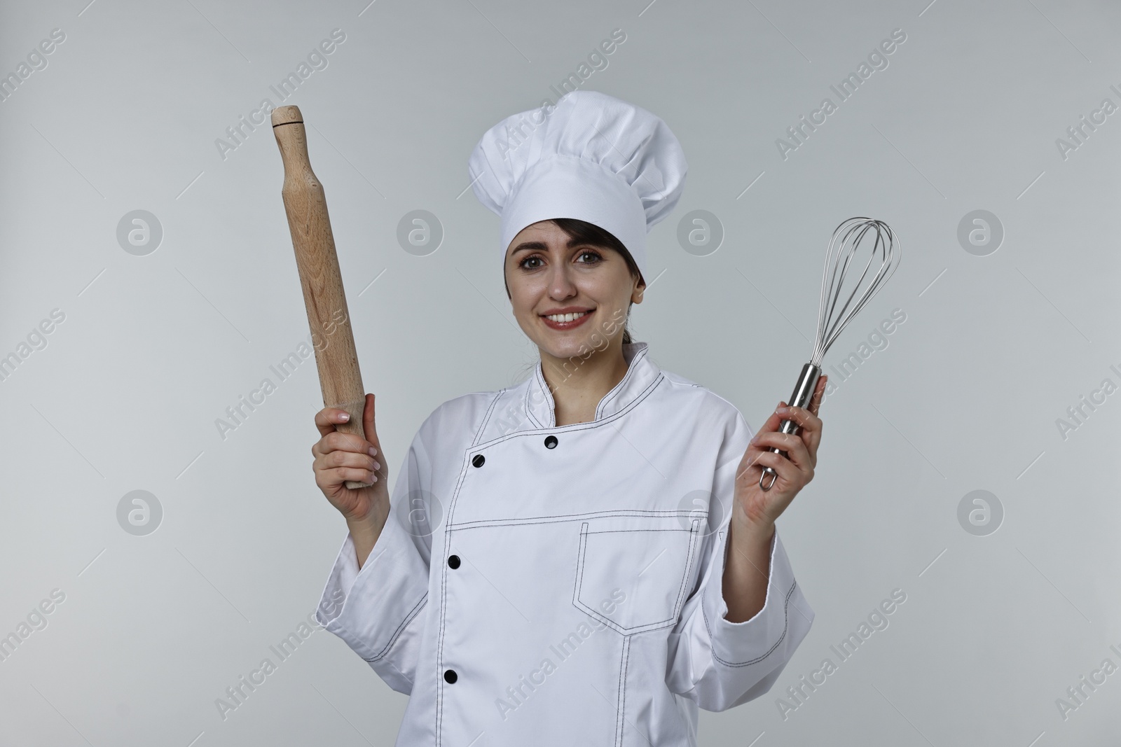 Photo of Professional chef with rolling pin and whisk on light grey background