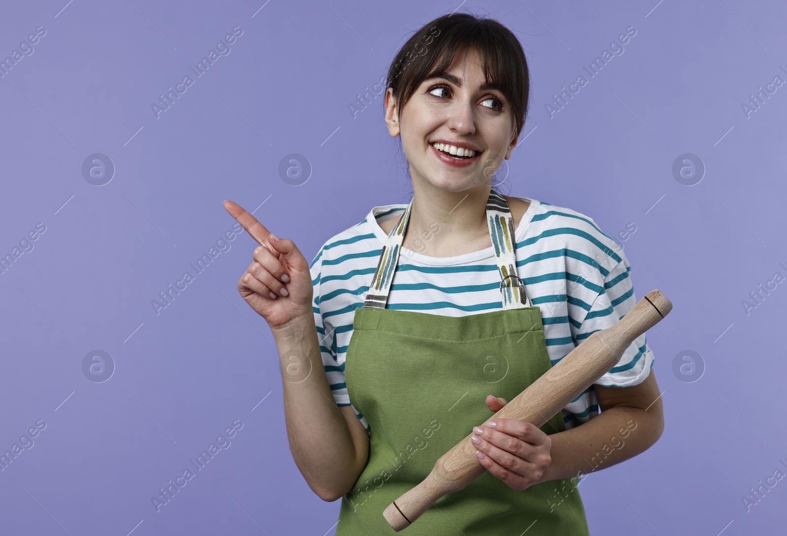 Photo of Woman with rolling pin pointing at something on violet background