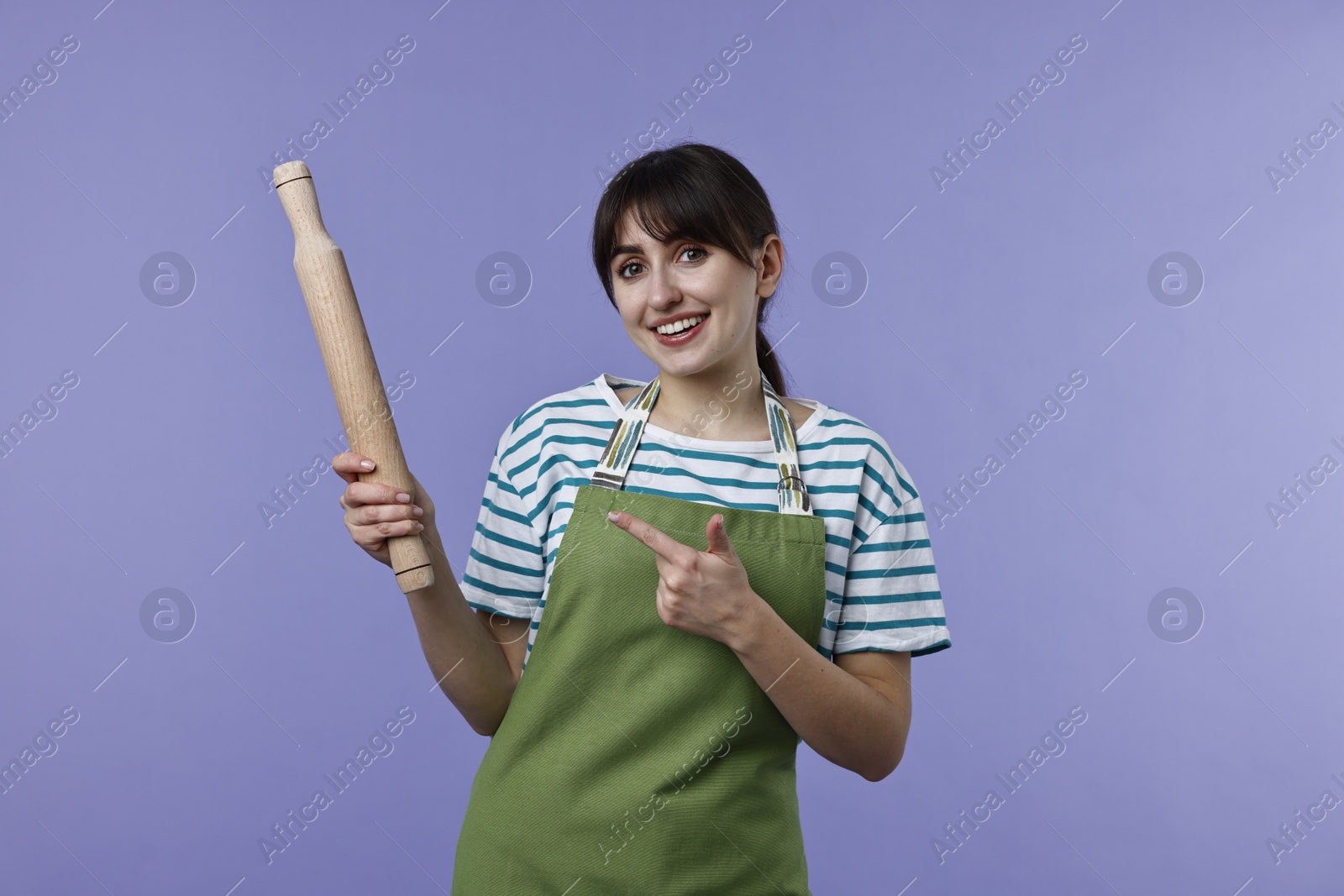 Photo of Happy woman pointing at rolling pin on violet background