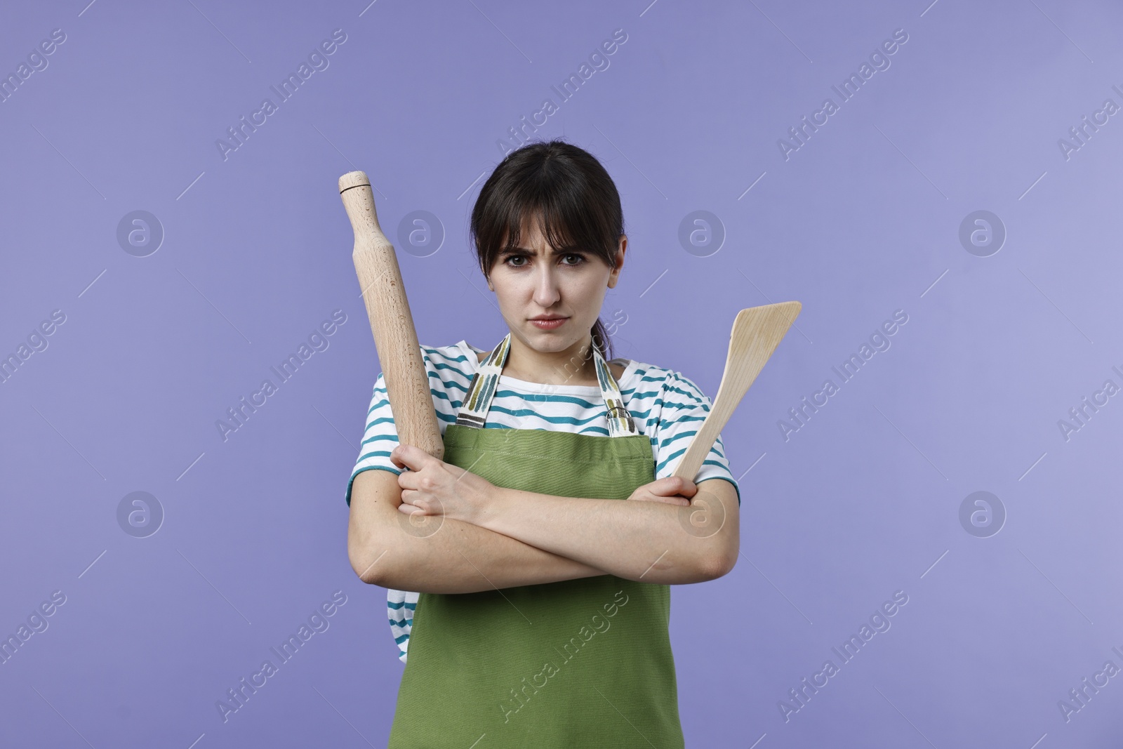 Photo of Angry woman with rolling pin and turner on violet background