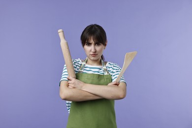 Photo of Angry woman with rolling pin and turner on violet background