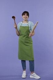 Photo of Woman with rolling pin and ladle on violet background