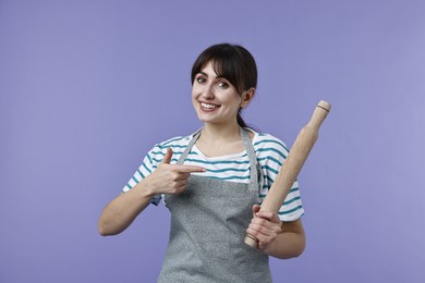 Photo of Happy woman pointing at rolling pin on violet background