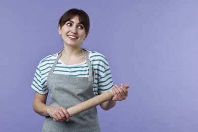 Photo of Happy woman with rolling pin on violet background. Space for text