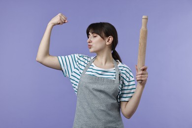 Photo of Woman with rolling pin kissing bicep on violet background