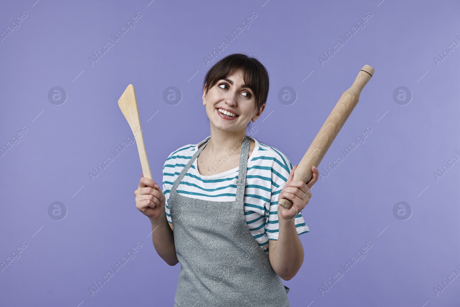 Photo of Happy woman with rolling pin and turner on violet background