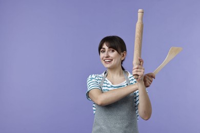 Photo of Happy woman with rolling pin and turner on violet background. Space for text